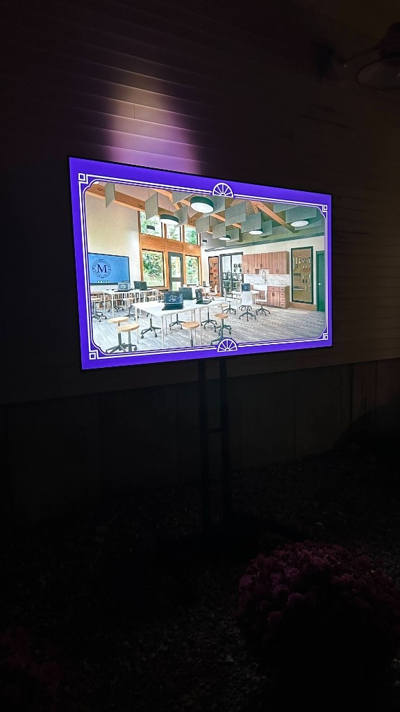 A 75-inch on a rolling stand showing a classroom rendering of the new wing.