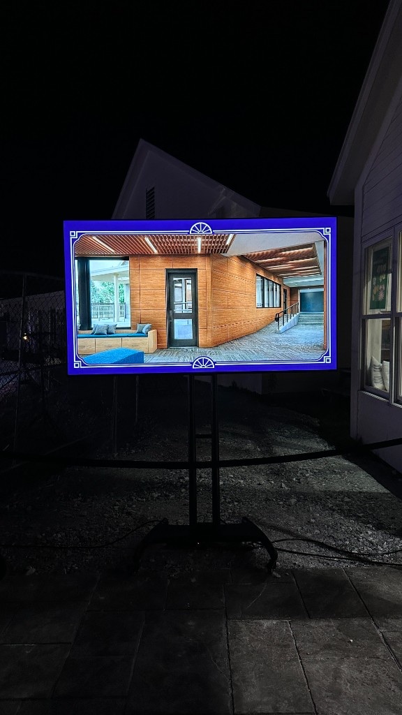 A 75-inch on a rolling stand showing an exterior rendering of the new building.