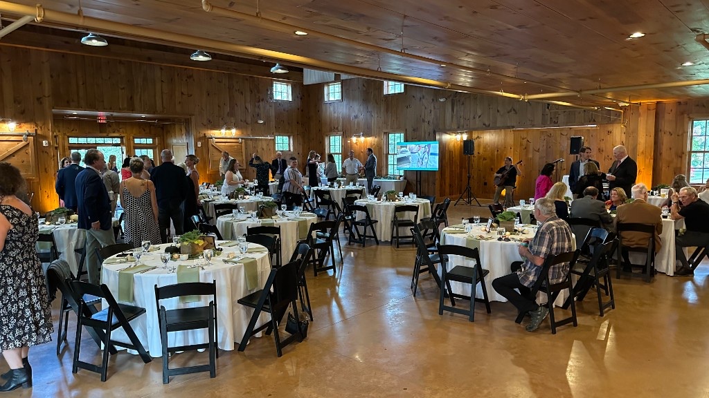 Guests in the Celebration Barn during cocktails, with the monitor visible across the room.