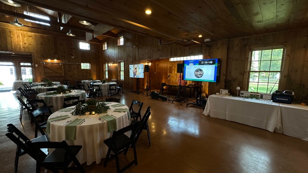 The Celebration Barn set before guests, two monitors live and uplights on the wood.