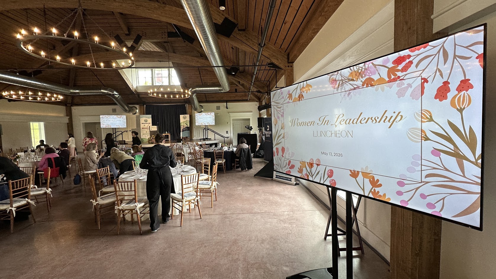 Women in Leadership Luncheon 2026 — room setup with Woman of the Year Award slide on 75-inch display.